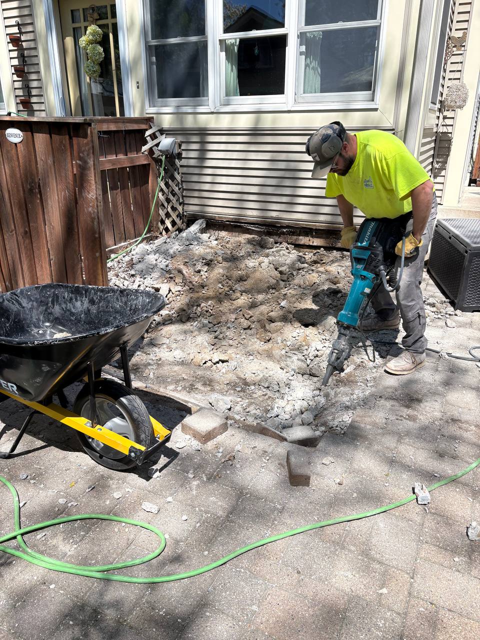 Crew member in hi-vis vest jackhammering residential concrete pad, Minneapolis MN