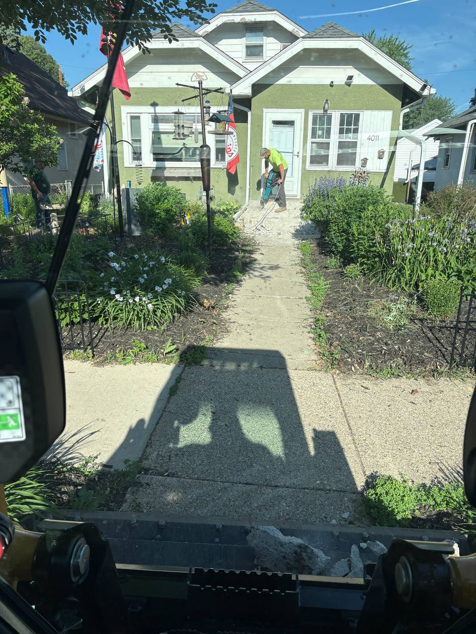 Crew jackhammering concrete sidewalk in front of green Minneapolis craftsman home
